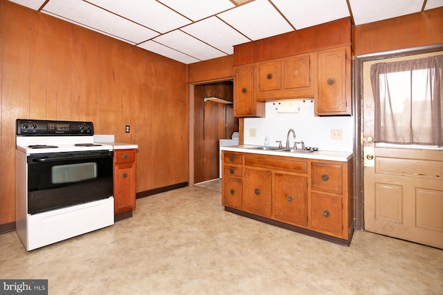 kitchen with wooden walls, light countertops, range with electric stovetop, brown cabinetry, and a sink