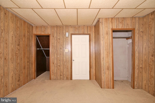 unfurnished bedroom with a closet, carpet flooring, wood walls, and a walk in closet