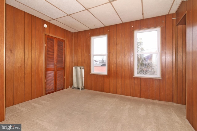 unfurnished room featuring radiator, wood walls, and carpet flooring