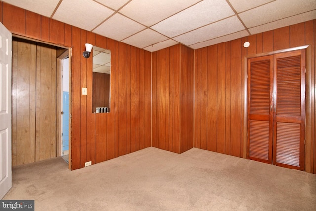 carpeted spare room featuring wooden walls and a paneled ceiling