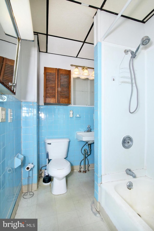 bathroom featuring tile patterned floors, toilet, washtub / shower combination, and tile walls