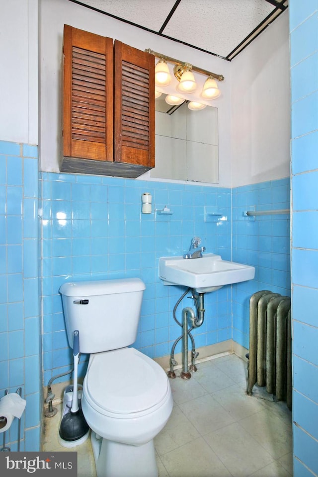 half bath with a wainscoted wall, toilet, radiator heating unit, tile walls, and a sink