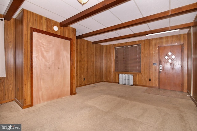 carpeted empty room with beam ceiling, wooden walls, and radiator