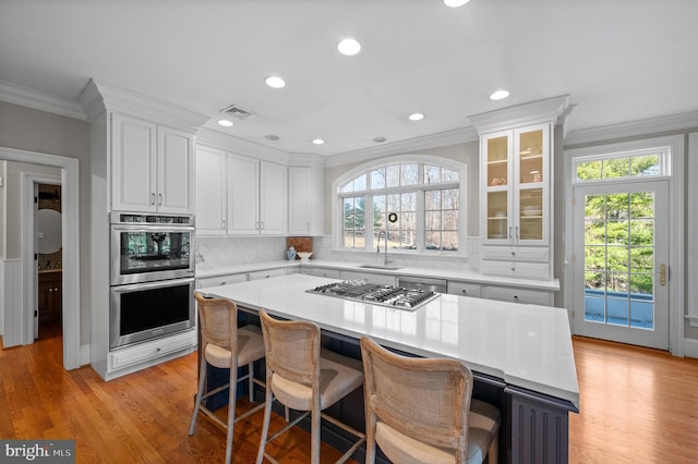 kitchen featuring ornamental molding, a sink, appliances with stainless steel finishes, white cabinetry, and tasteful backsplash