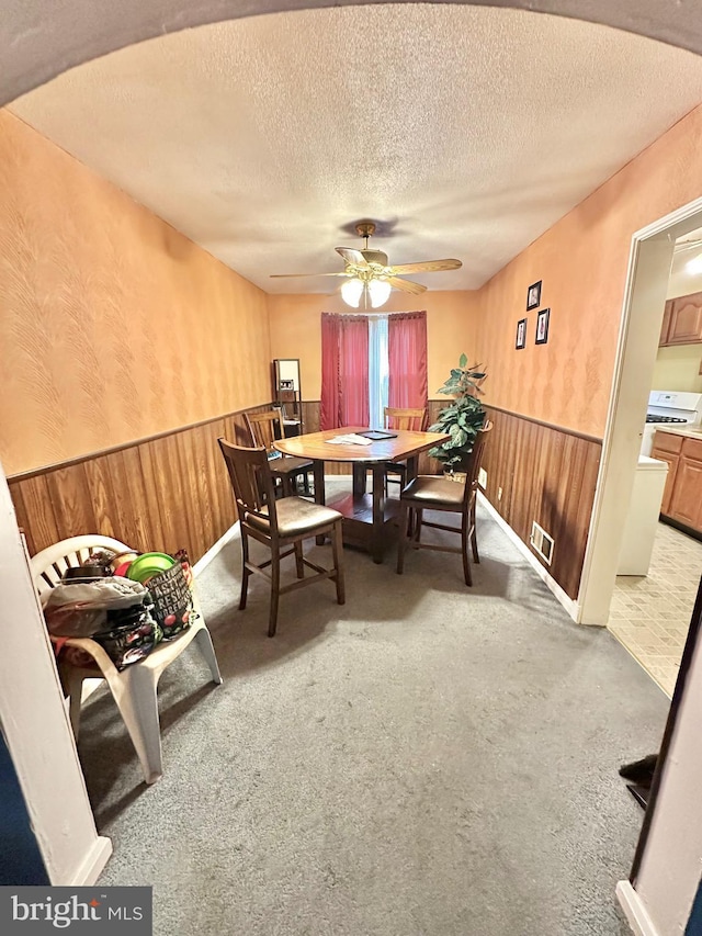 carpeted dining area featuring a wainscoted wall, ceiling fan, wood walls, and a textured ceiling