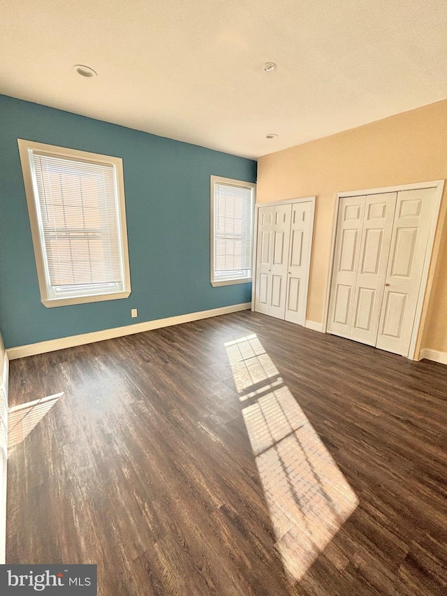 unfurnished bedroom featuring baseboards, two closets, and wood finished floors