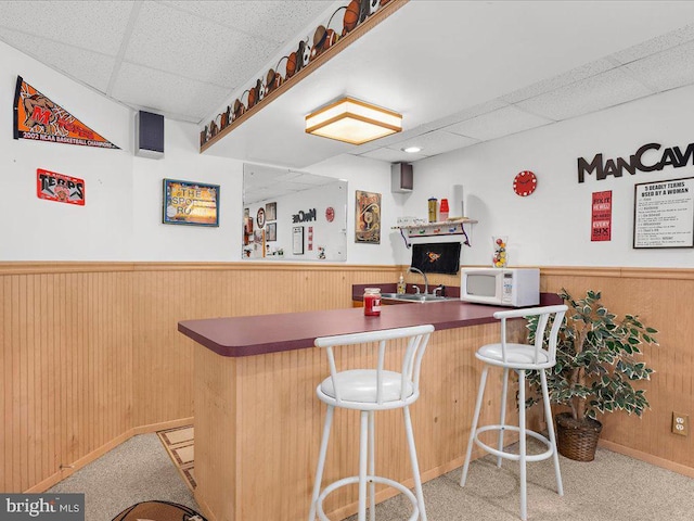 bar featuring white microwave, wainscoting, and a sink