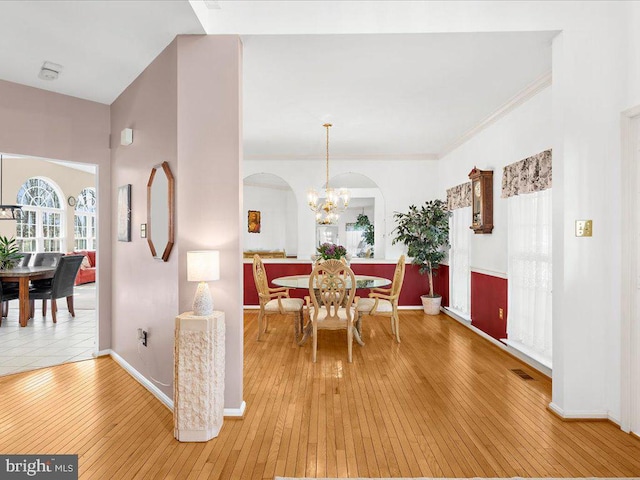 dining space featuring ornamental molding, arched walkways, light wood-style floors, an inviting chandelier, and baseboards