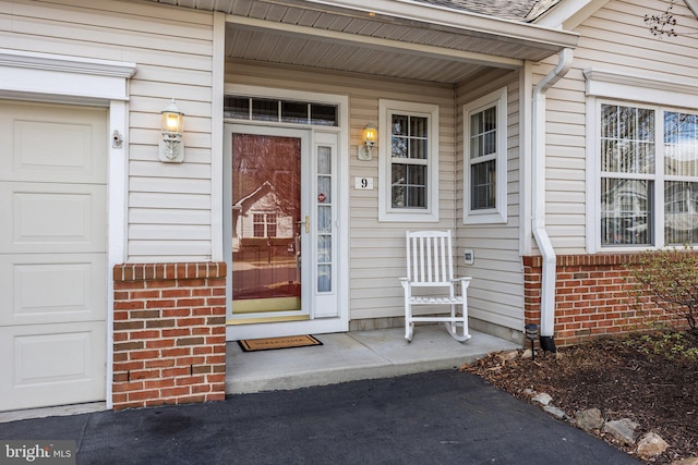 view of exterior entry with brick siding, a porch, and an attached garage