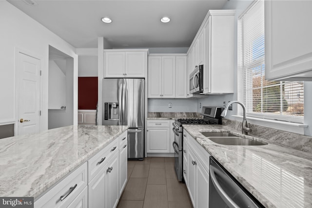 kitchen with light stone counters, dark tile patterned flooring, a sink, appliances with stainless steel finishes, and white cabinetry