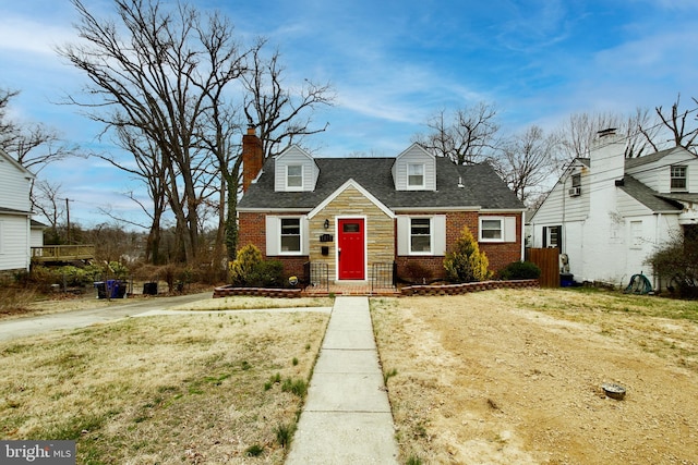 cape cod house with brick siding, a chimney, and a shingled roof