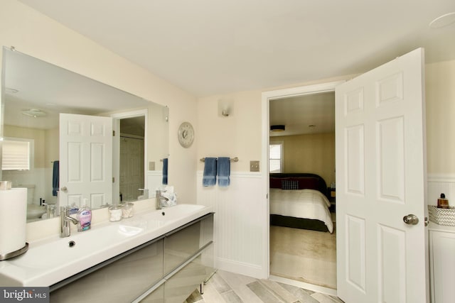 ensuite bathroom with ensuite bath, double vanity, a wainscoted wall, and a sink