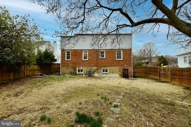 rear view of house featuring cooling unit, brick siding, a fenced backyard, and a yard