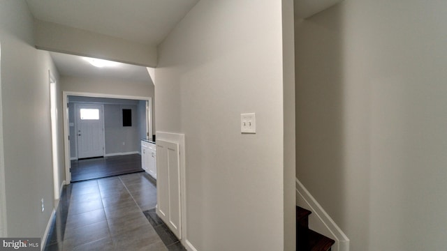 hallway featuring dark tile patterned floors, stairs, and baseboards