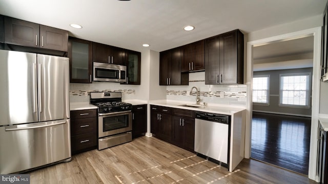 kitchen with a sink, stainless steel appliances, light countertops, dark brown cabinets, and light wood-type flooring