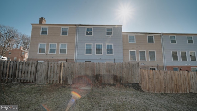 back of house featuring a yard, a fenced backyard, and a chimney