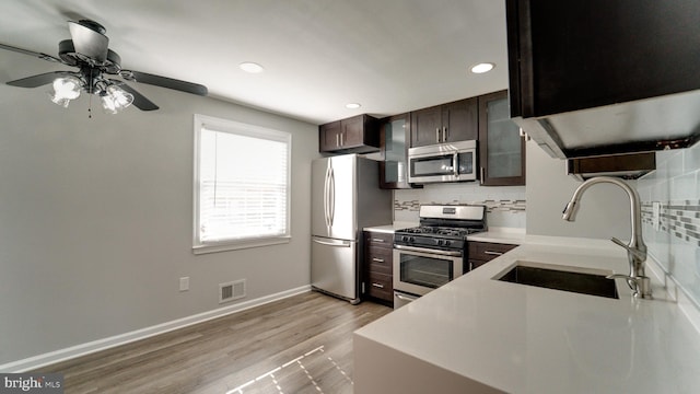 kitchen with a sink, decorative backsplash, light countertops, dark brown cabinets, and appliances with stainless steel finishes