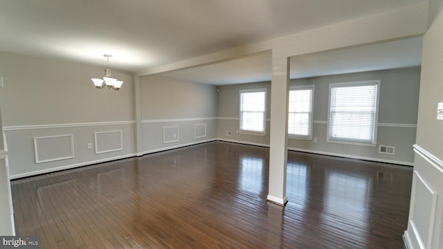 empty room featuring a notable chandelier, visible vents, a wainscoted wall, and wood finished floors