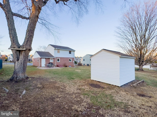 rear view of property featuring an outbuilding, a patio, brick siding, a yard, and a storage unit