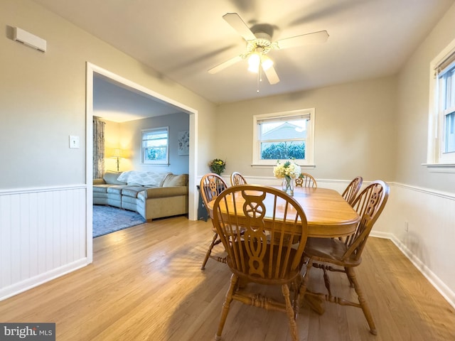 dining space with a ceiling fan, a wainscoted wall, and light wood-style flooring