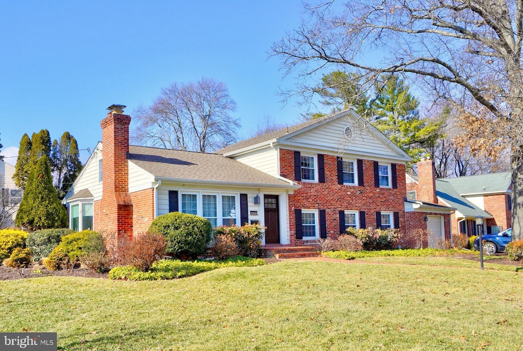 view of front facade with brick siding, an attached garage, a chimney, and a front yard