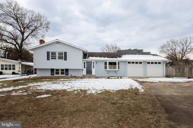 split level home with a garage, driveway, a chimney, and fence