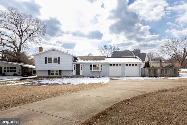 split level home featuring a garage, driveway, a chimney, and fence