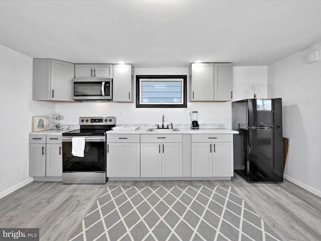 kitchen featuring light wood finished floors, baseboards, appliances with stainless steel finishes, light countertops, and a sink