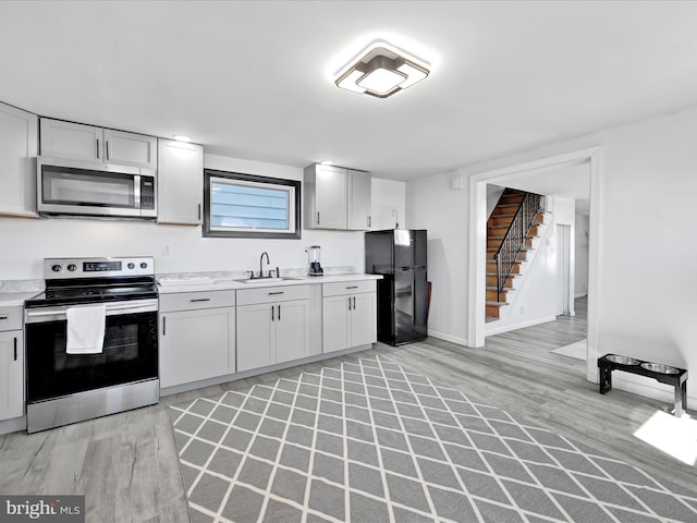 kitchen with stainless steel appliances, a sink, baseboards, light wood-style floors, and light countertops