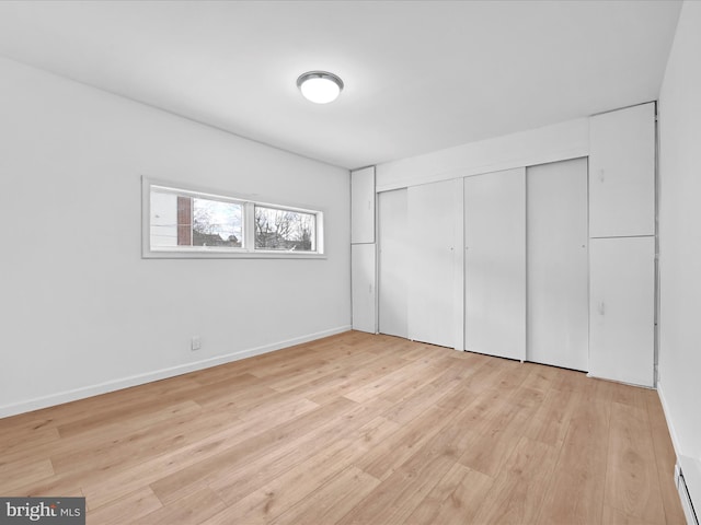 unfurnished bedroom featuring baseboard heating, a closet, light wood-style flooring, and baseboards