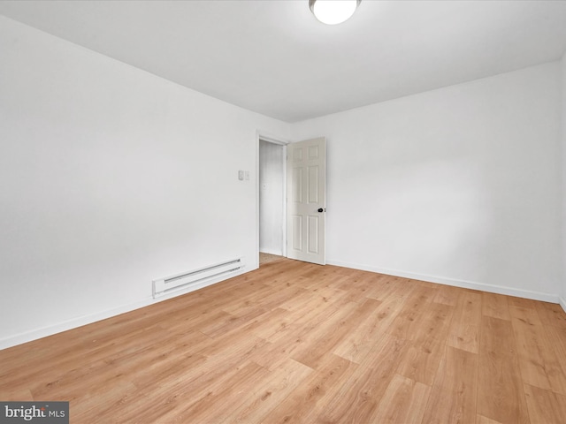 empty room featuring a baseboard heating unit, baseboards, and wood finished floors