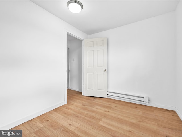 empty room featuring baseboard heating, wood finished floors, and baseboards