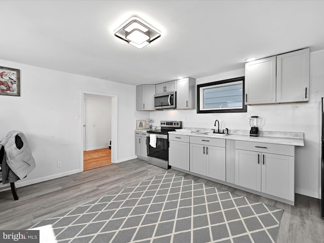 kitchen with baseboards, stainless steel appliances, light countertops, light wood-style floors, and a sink