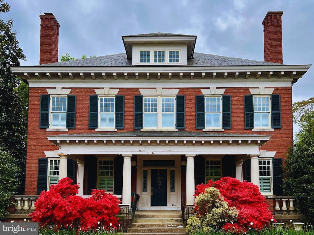 georgian-style home with a chimney, a porch, and brick siding