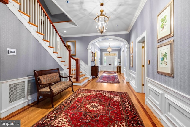 entryway with arched walkways, a notable chandelier, light wood-type flooring, and a wainscoted wall