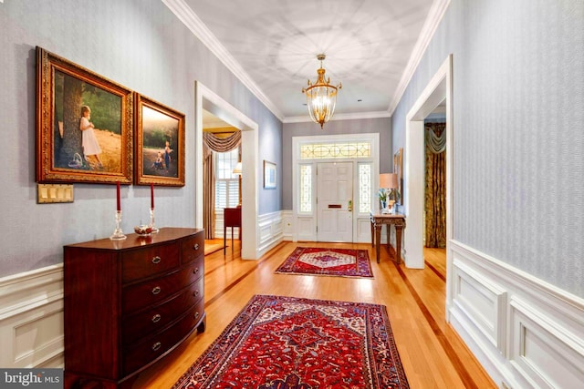 foyer entrance featuring light wood finished floors, an inviting chandelier, crown molding, a decorative wall, and wainscoting