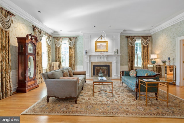 living area with a glass covered fireplace, wood finished floors, ornamental molding, and wallpapered walls