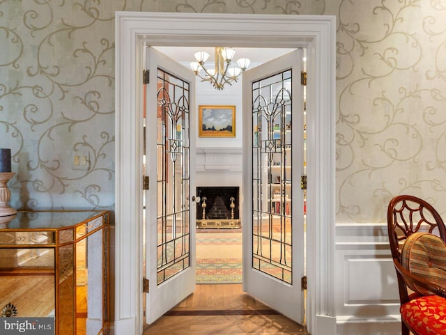 entryway with a notable chandelier, wallpapered walls, and wood finished floors