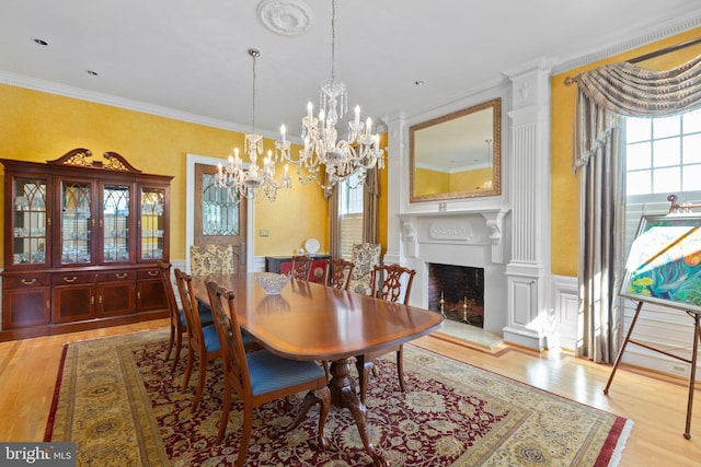 dining area with light wood-style floors, a fireplace with raised hearth, a chandelier, and ornamental molding