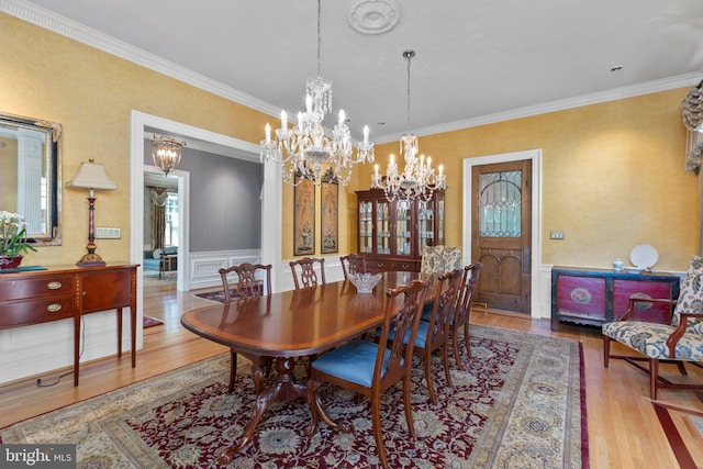 dining room with ornamental molding, wood finished floors, wainscoting, and a chandelier