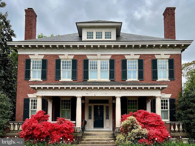 colonial house featuring brick siding, covered porch, and a chimney