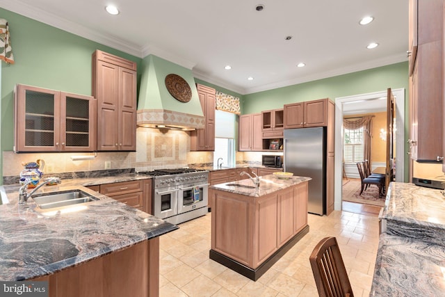 kitchen featuring light stone counters, custom exhaust hood, a sink, premium appliances, and a wealth of natural light