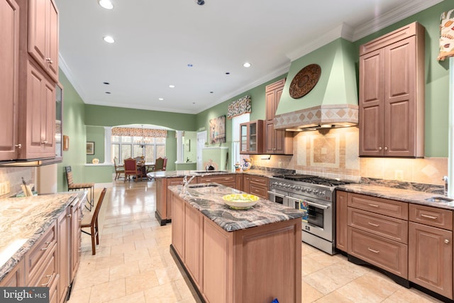 kitchen featuring light stone countertops, arched walkways, stainless steel stove, custom range hood, and backsplash