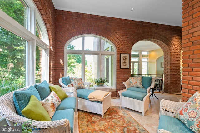 living room with arched walkways, light tile patterned floors, and brick wall