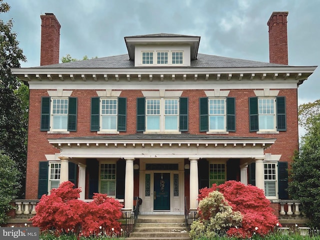 colonial inspired home featuring brick siding, a porch, and a chimney