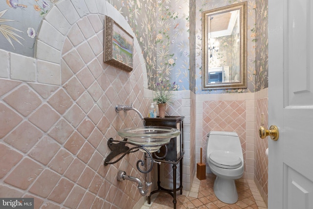 bathroom with wallpapered walls, a sink, wainscoting, tile patterned floors, and toilet