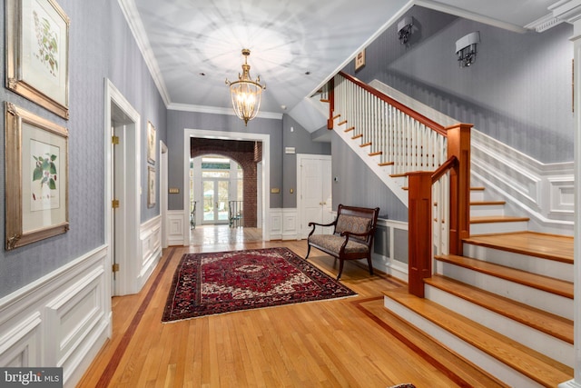 foyer featuring stairway, arched walkways, ornamental molding, hardwood / wood-style flooring, and a chandelier