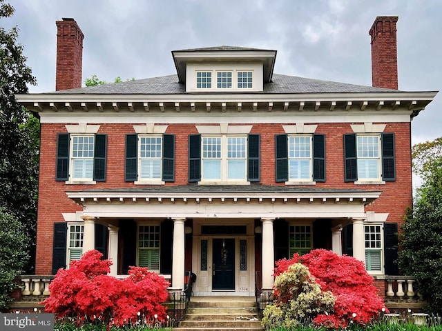 colonial house featuring brick siding, a porch, and a chimney