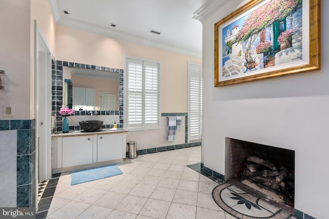 bathroom with visible vents, a fireplace with flush hearth, vanity, ornamental molding, and tile walls