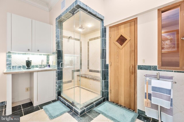 full bathroom with tile patterned flooring, a shower stall, ornamental molding, tile walls, and a sink